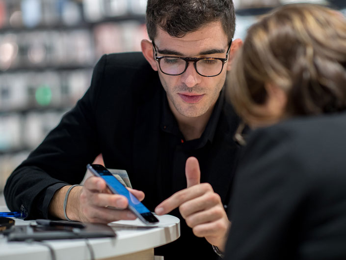 Un conseiller en magasin Orange aide un client à paramétrer son nouveau téléphone mobile